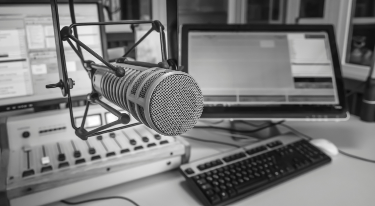 Microphone de studio de radio devant un écran d'ordinateur et une table de mixage, utilisé pour l'enregistrement ou la diffusion.