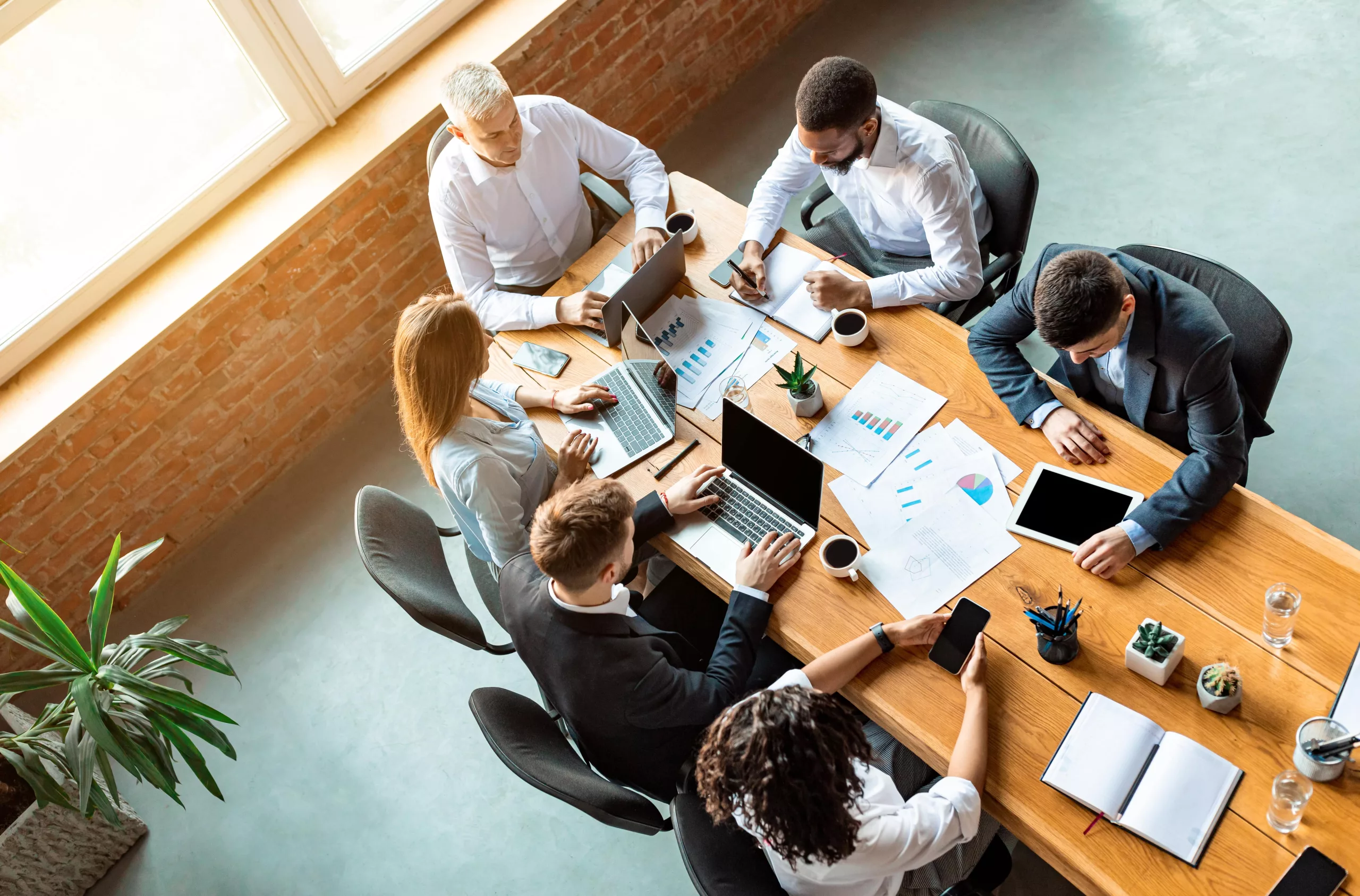 Réunion de travail entre collègues autour d'une grande table en bois, avec des ordinateurs portables, des graphiques et des notes, illustrant une discussion stratégique sur la gestion des risques.